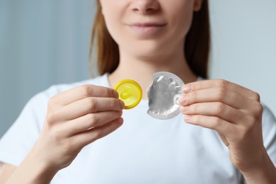 Woman holding unwrapped condom indoors, closeup. Safe sex