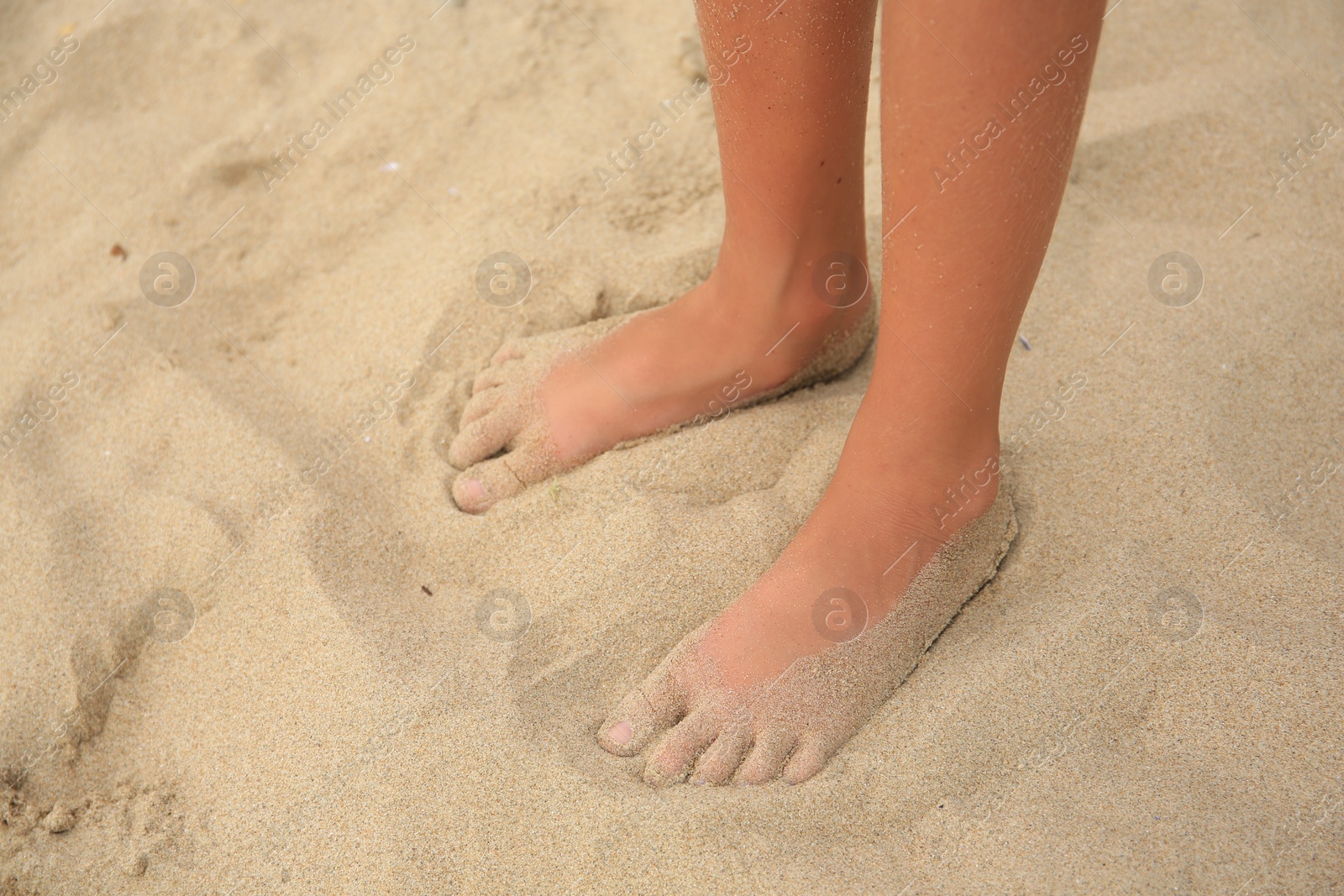 Photo of Little girl standing on sandy beach, closeup