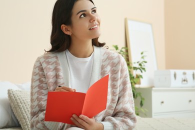 Young woman writing message in greeting card indoors, space for text