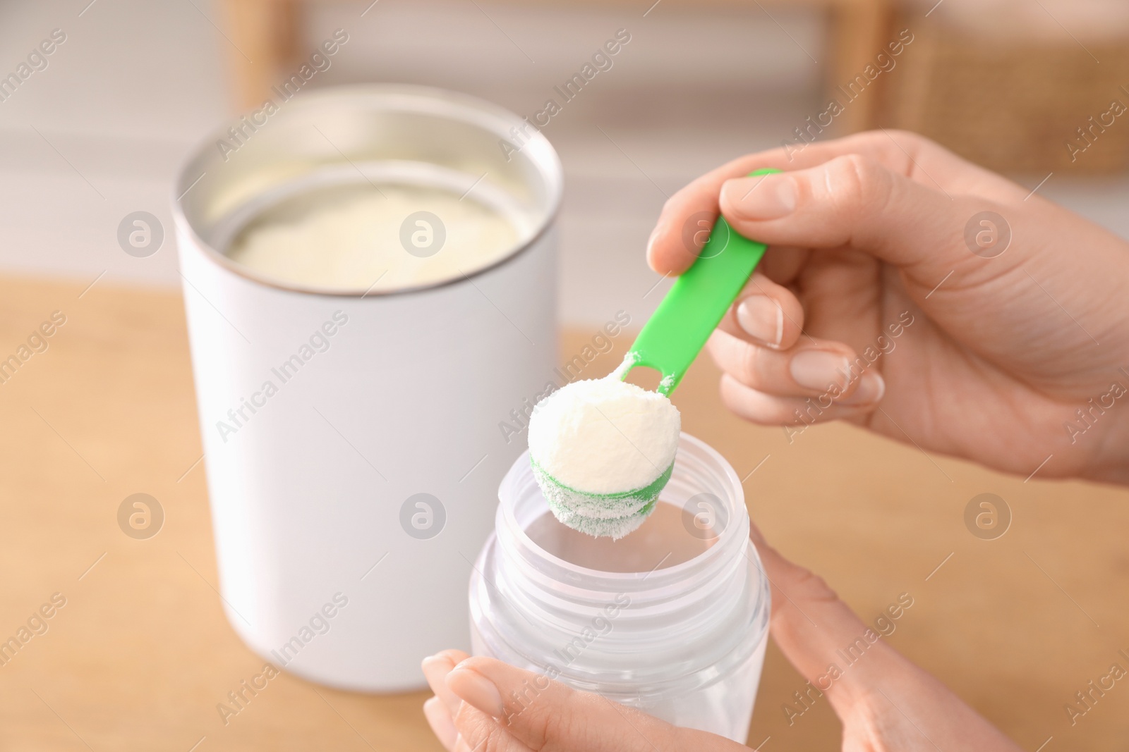 Photo of Woman preparing infant formula at table indoors, closeup. Baby milk