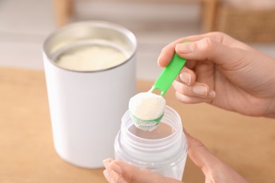 Photo of Woman preparing infant formula at table indoors, closeup. Baby milk