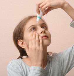 Image of Conjunctivitis. Girl using eye drops on beige background
