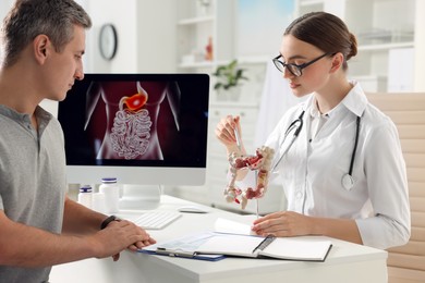 Photo of Gastroenterologist with anatomical model of large intestine consulting patient at table in clinic