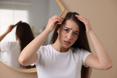 Emotional woman with comb examining her hair and scalp indoors. Dandruff problem