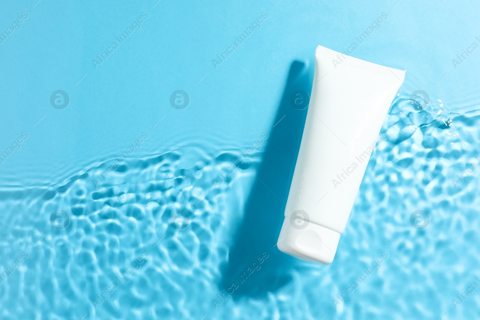 Photo of Tube with moisturizing cream in water on light blue background, top view. Space for text