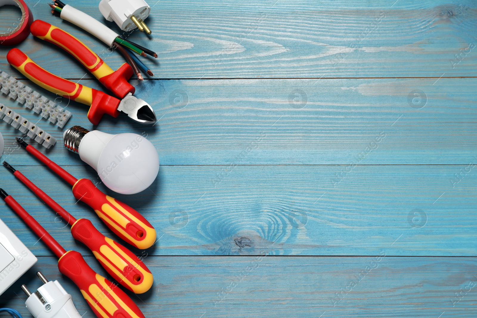 Photo of Set of electrician's tools and accessories on light blue wooden table, flat lay. Space for text