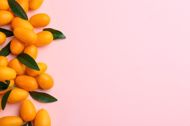 Photo of Fresh ripe kumquats with green leaves on pink background, flat lay. Space for text
