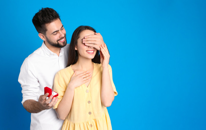 Man with engagement ring making marriage proposal to girlfriend on blue background