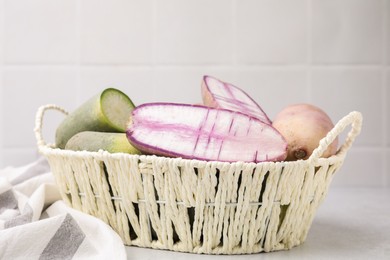 Purple and green daikon radishes in wicker basket on light grey table