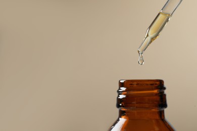 Photo of Dripping hydrophilic oil into bottle on dark beige background, closeup. Space for text