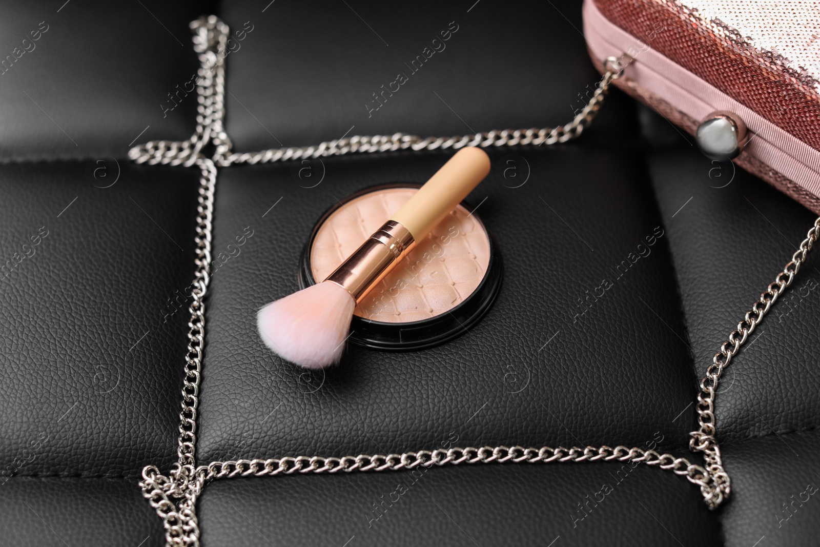 Photo of Powder, brush and handbag on black leather background
