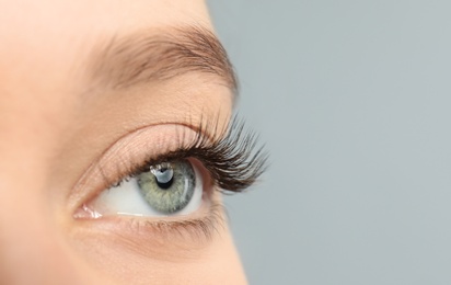 Young woman with beautiful long eyelashes on gray background, closeup. Extension procedure