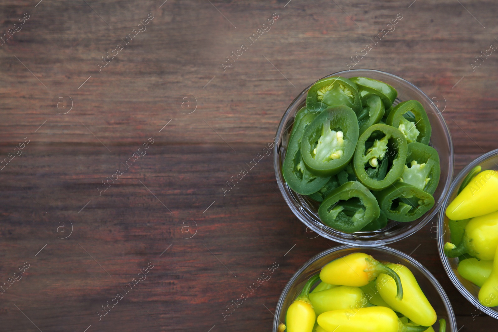 Photo of Pickled green and yellow jalapeno peppers on wooden table, flat lay. Space for text