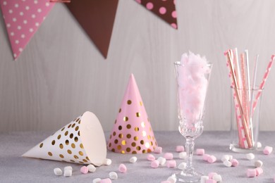 Photo of Tasty cotton candy cocktail in glass, festive decor and marshmallows on gray table against light wooden wall