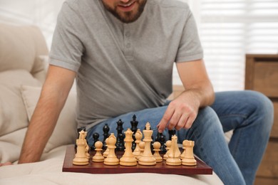 Man playing chess alone on sofa at home, closeup