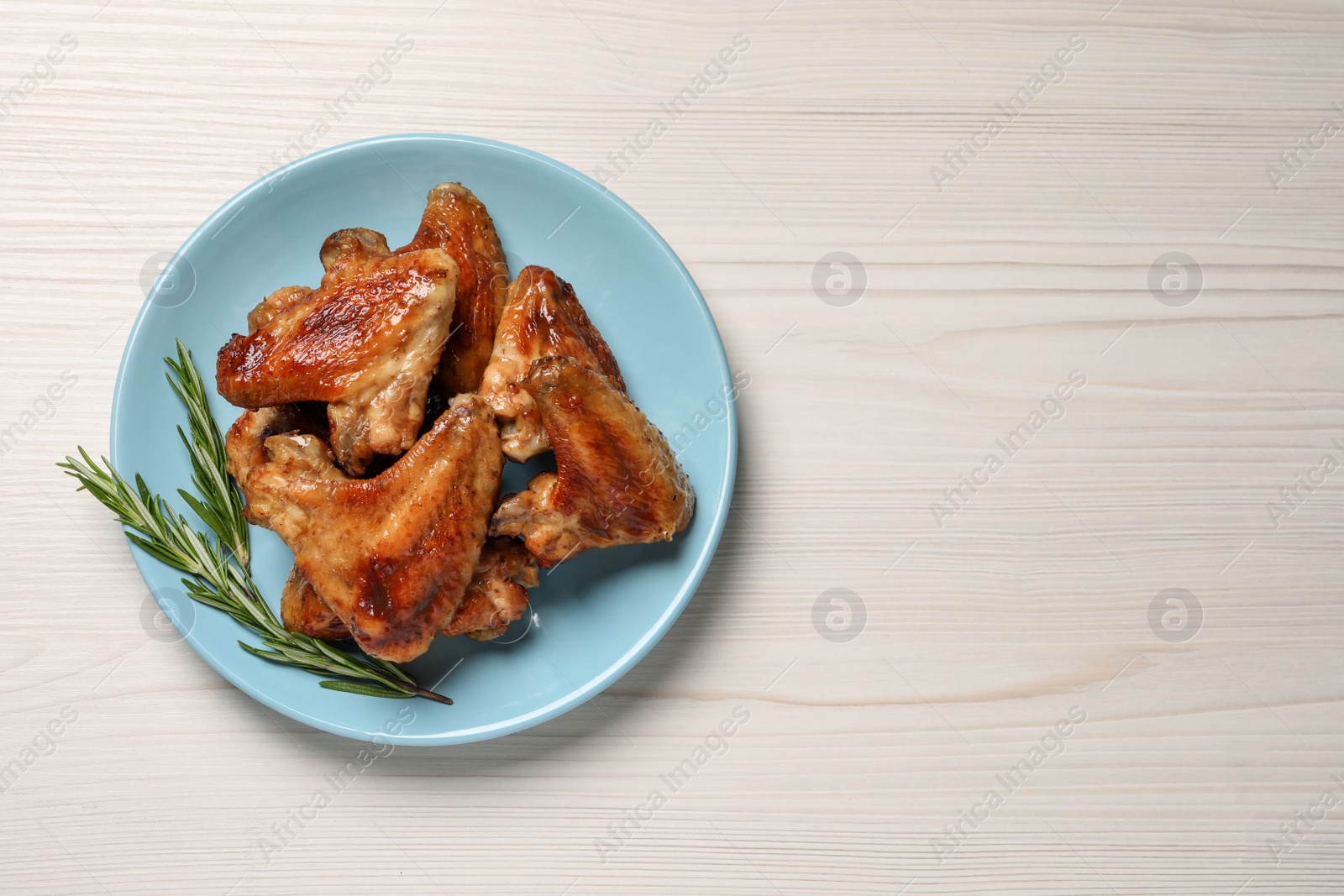 Photo of Plate with delicious fried chicken wings and sprig of rosemary on white wooden table, top view. Space for text