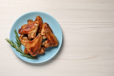 Plate with delicious fried chicken wings and sprig of rosemary on white wooden table, top view. Space for text