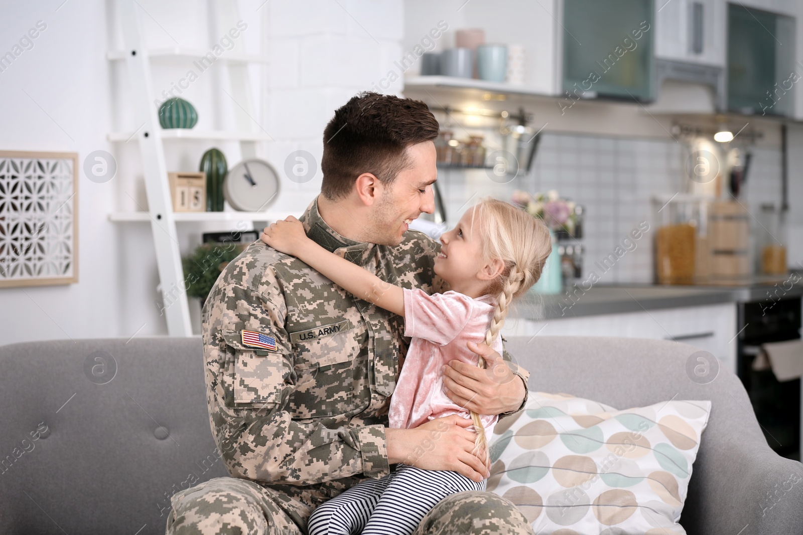 Photo of Young man in military uniform with his little daughter on sofa at home