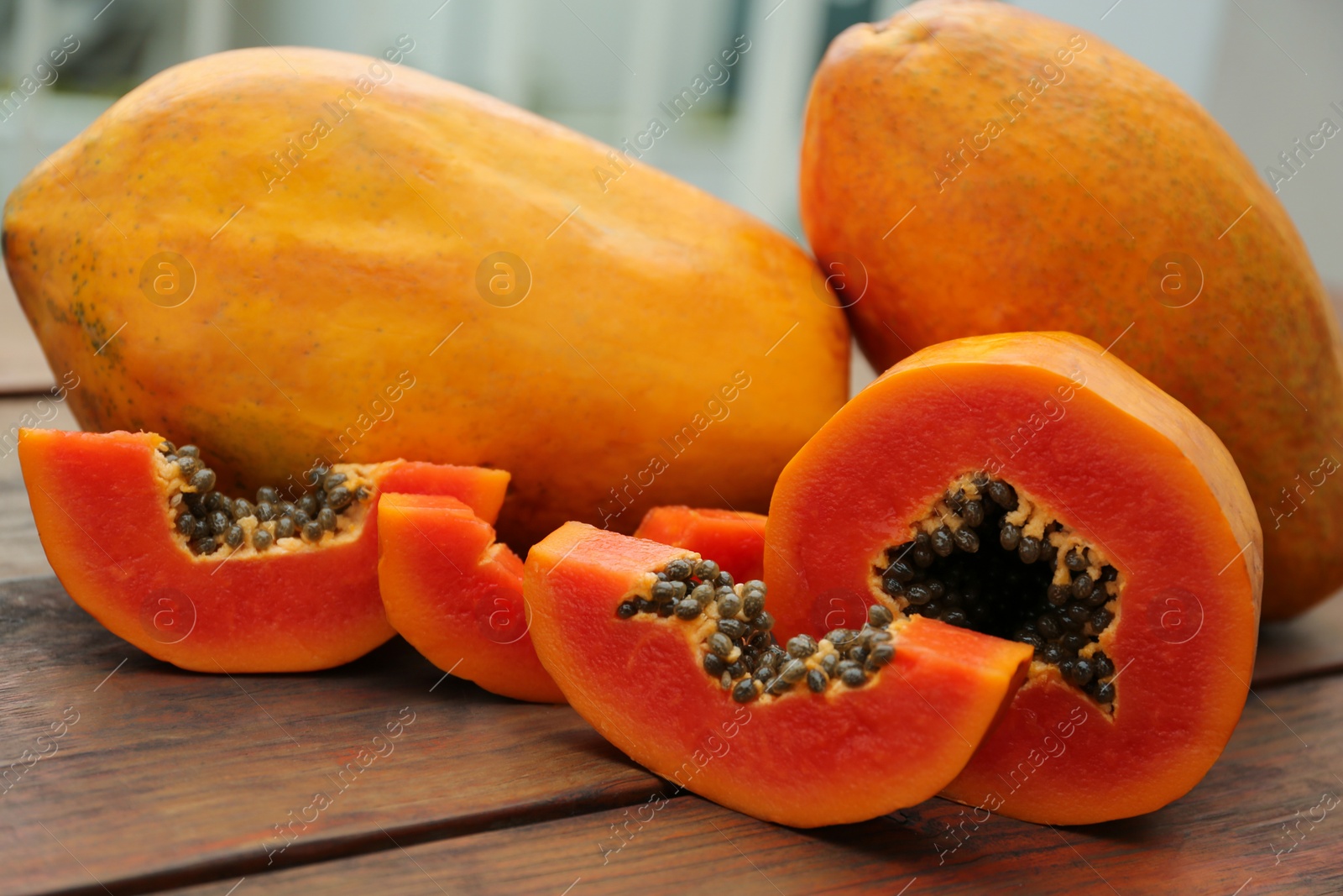 Photo of Ripe cut and whole papaya fruits on wooden table, closeup