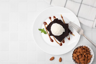 Photo of Tasty brownies served with ice cream and caramel sauce on white tiled table, flat lay. Space for text