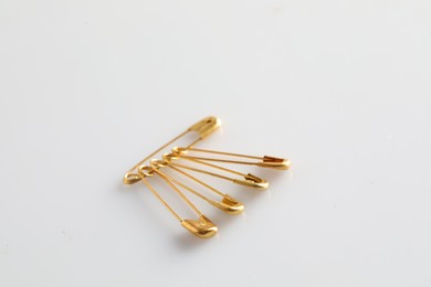 Photo of Golden safety pins on white background, space for text