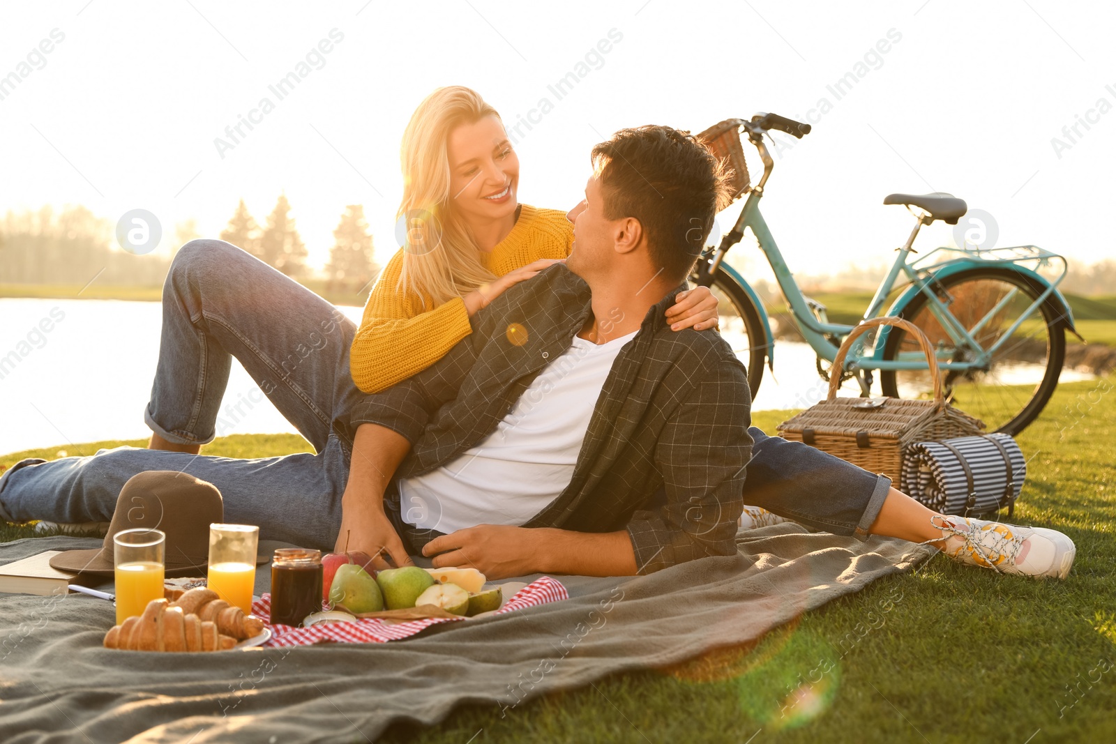 Photo of Happy young couple having picnic near lake on sunny day