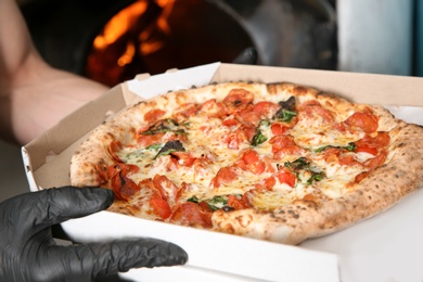 Photo of Chef holding delivery box with traditional oven baked Italian pizza in kitchen restaurant, closeup