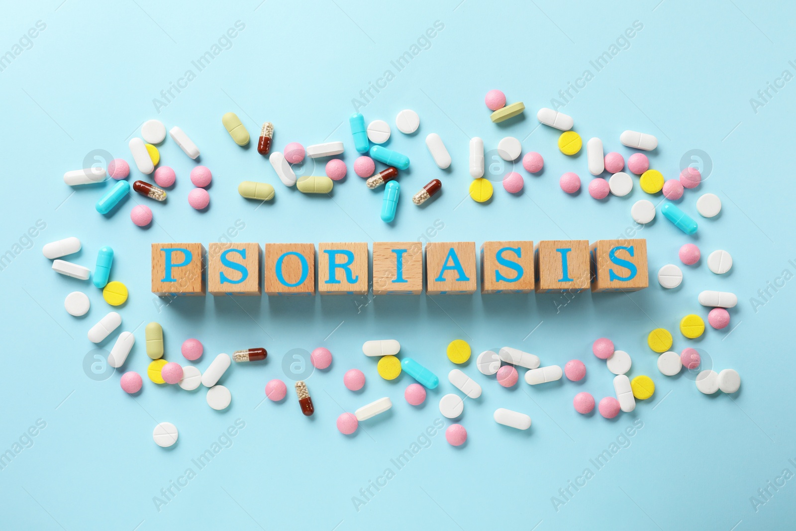 Photo of Word Psoriasis made of wooden cubes with letters and different pills on light blue background, flat lay