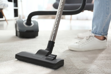 Photo of Janitor hoovering carpet with vacuum cleaner indoors, closeup
