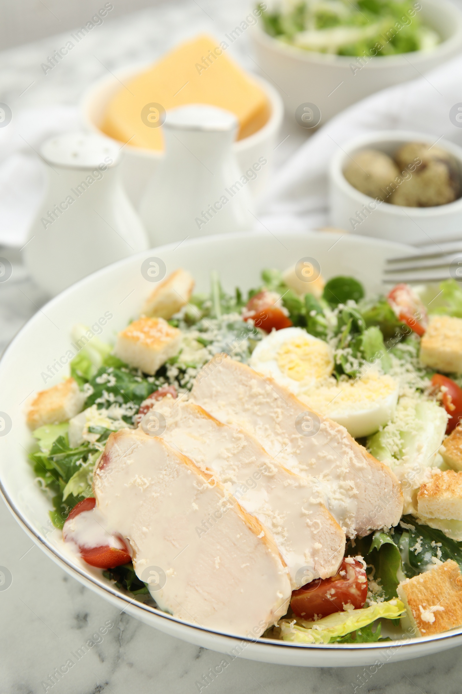 Photo of Delicious Caesar salad in bowl on white marble table, closeup