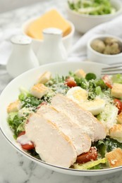 Photo of Delicious Caesar salad in bowl on white marble table, closeup