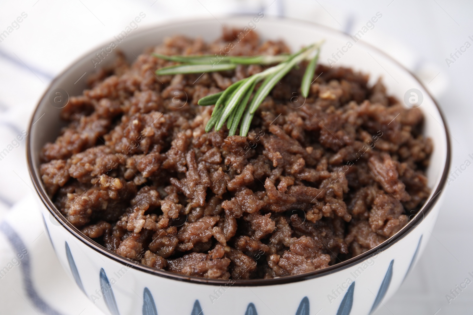 Photo of Fried ground meat in bowl and rosemary on table, closeup