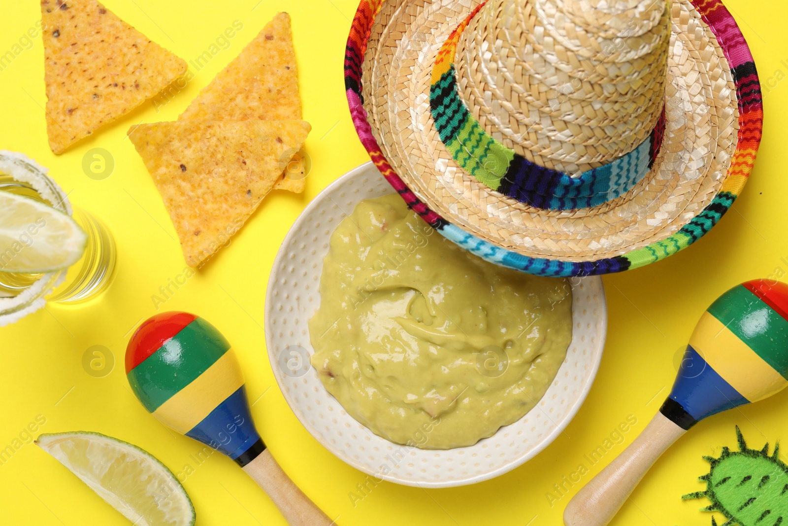 Photo of Mexican sombrero hat, nachos chips, guacamole, tequila and maracas on yellow background, flat lay