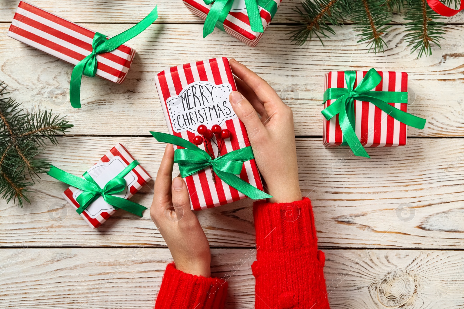 Photo of Woman holding Christmas gift box with green bow at white wooden table, top view