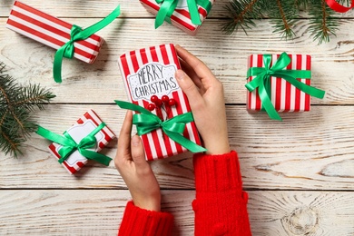 Woman holding Christmas gift box with green bow at white wooden table, top view