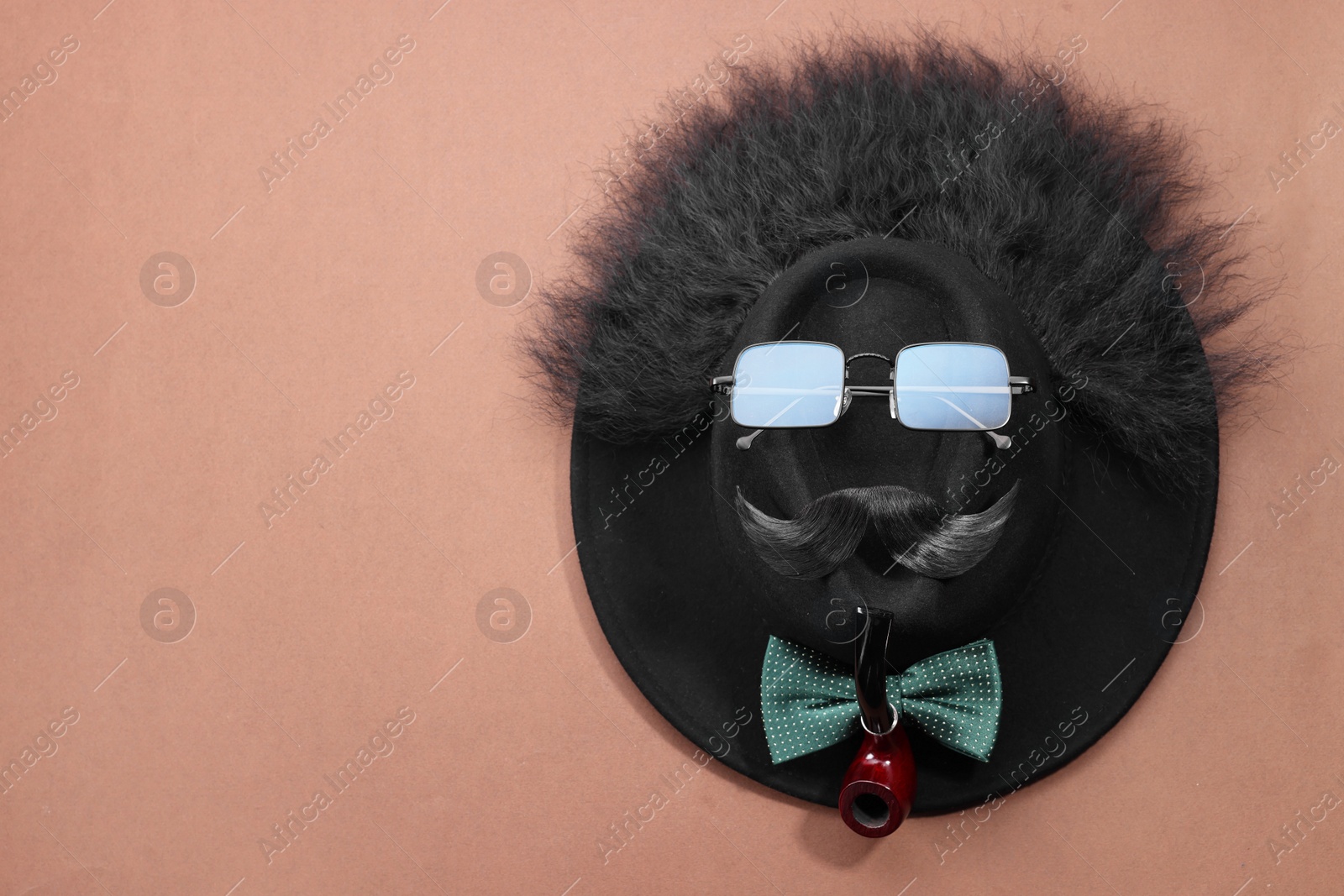 Photo of Man's face made of artificial mustache, sunglasses and hat on brown background, top view. Space for text