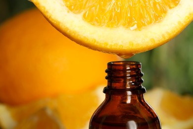 Photo of Dripping essential oil from orange into bottle on blurred background, closeup. Space for text