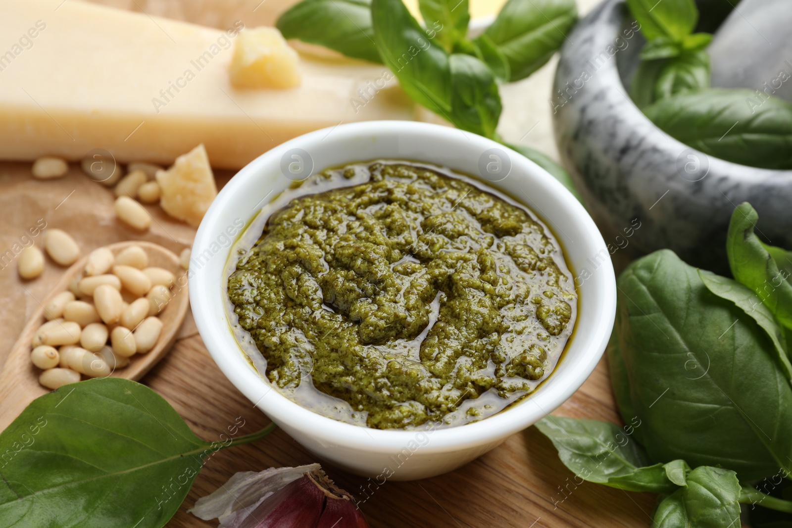 Photo of Tasty pesto sauce in bowl, basil, pine nuts and cheese on table, closeup