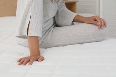 Photo of African American woman sitting on soft mattress in bedroom, closeup