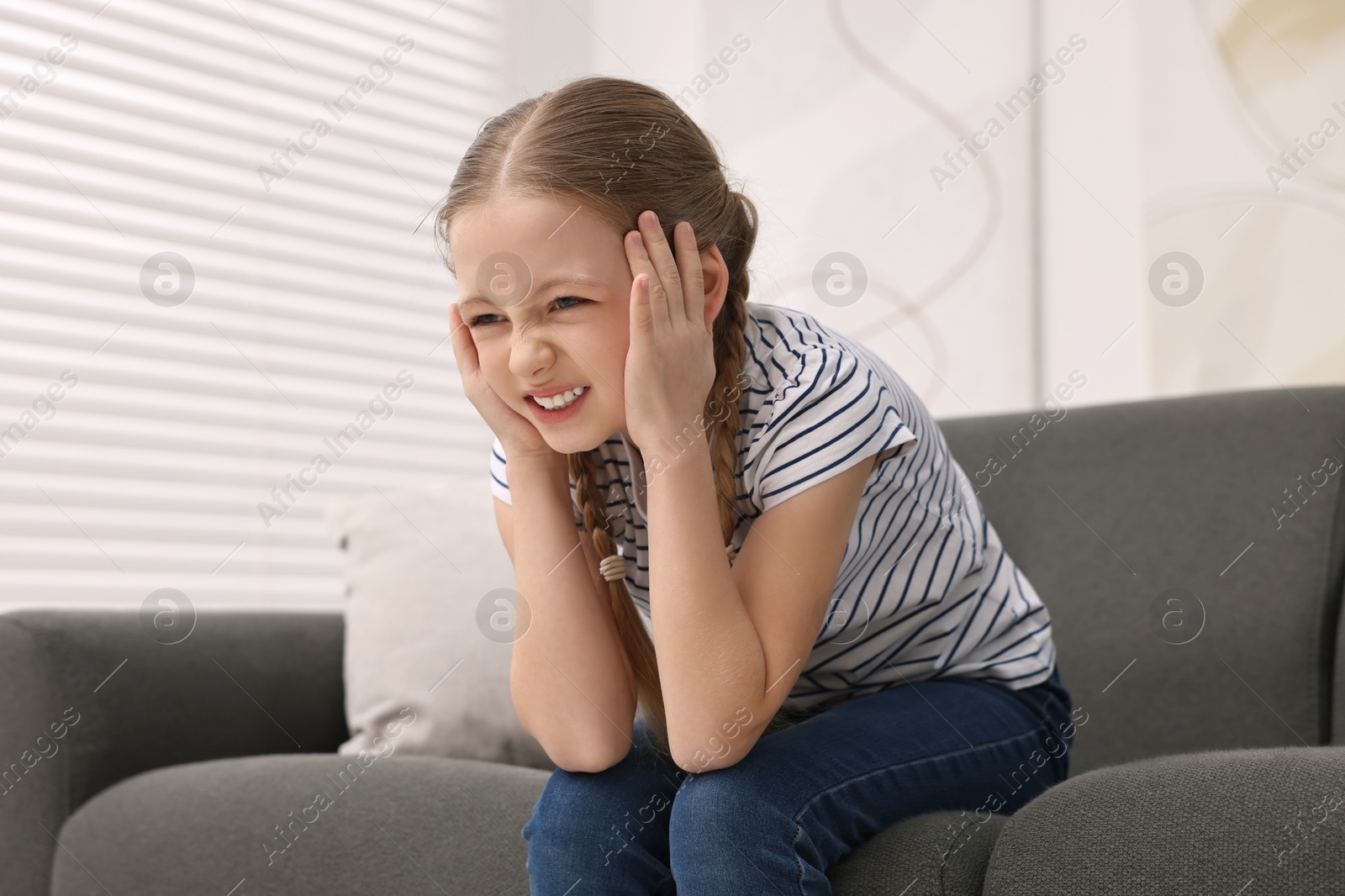 Photo of Little girl suffering from headache on sofa indoors