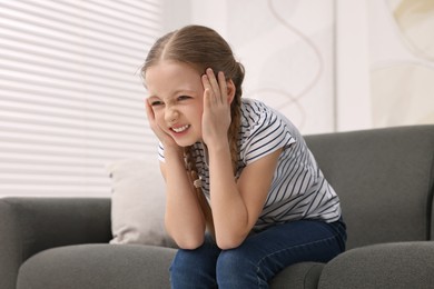 Photo of Little girl suffering from headache on sofa indoors