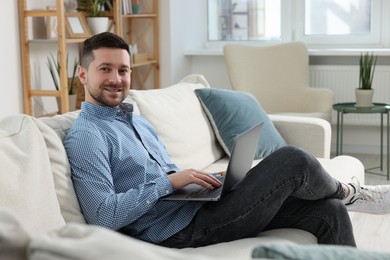 Happy man working with laptop on sofa at home
