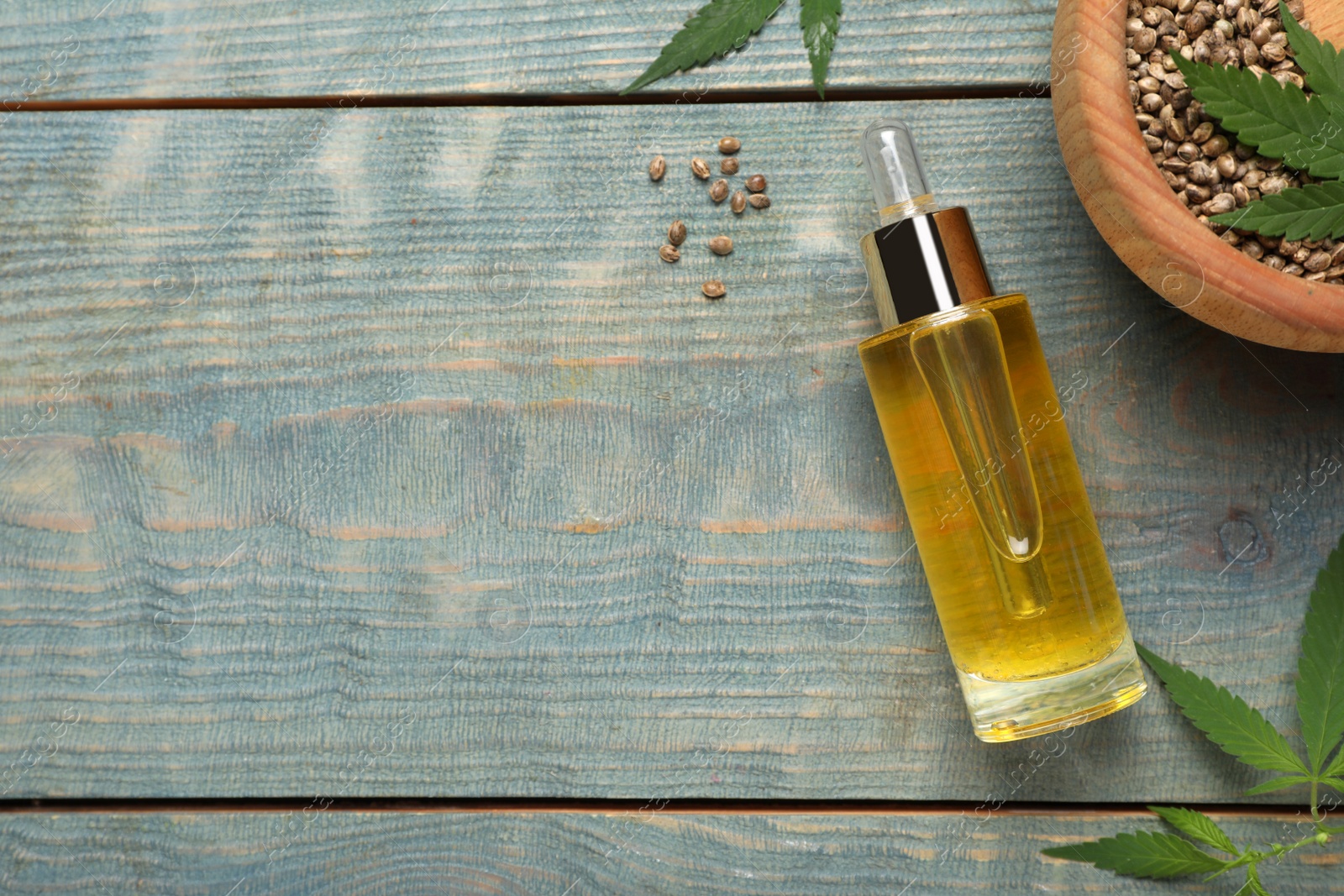 Photo of Hemp oil, seeds and leaves on light blue wooden table, flat lay. Space for text