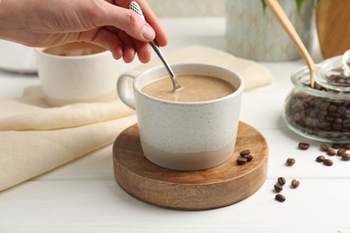 Photo of Woman stirring coffee with spoon at white wooden table, closeup