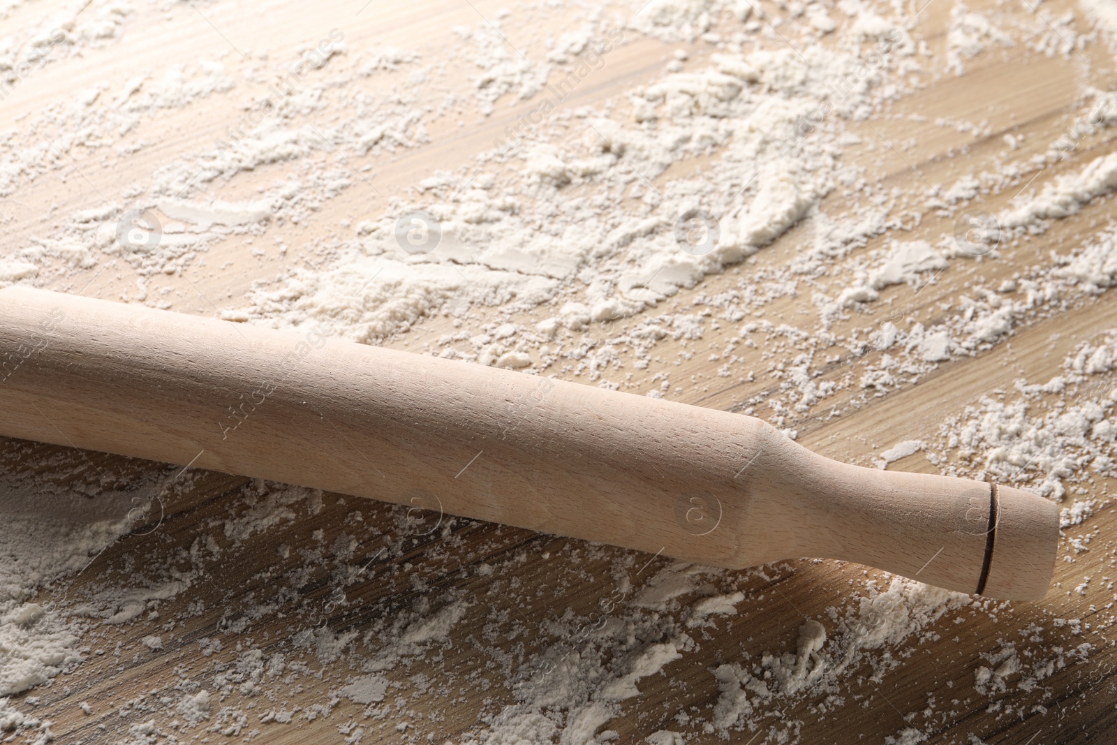 Photo of Scattered flour and rolling pin on wooden table, closeup