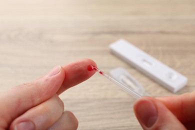 Laboratory testing. Woman taking blood sample from finger with pipette at table, closeup