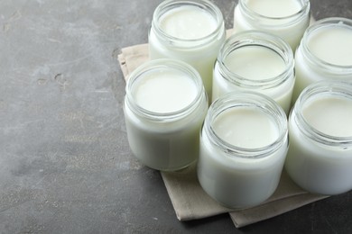 Photo of Tasty yogurt in glass jars on grey table. Space for text