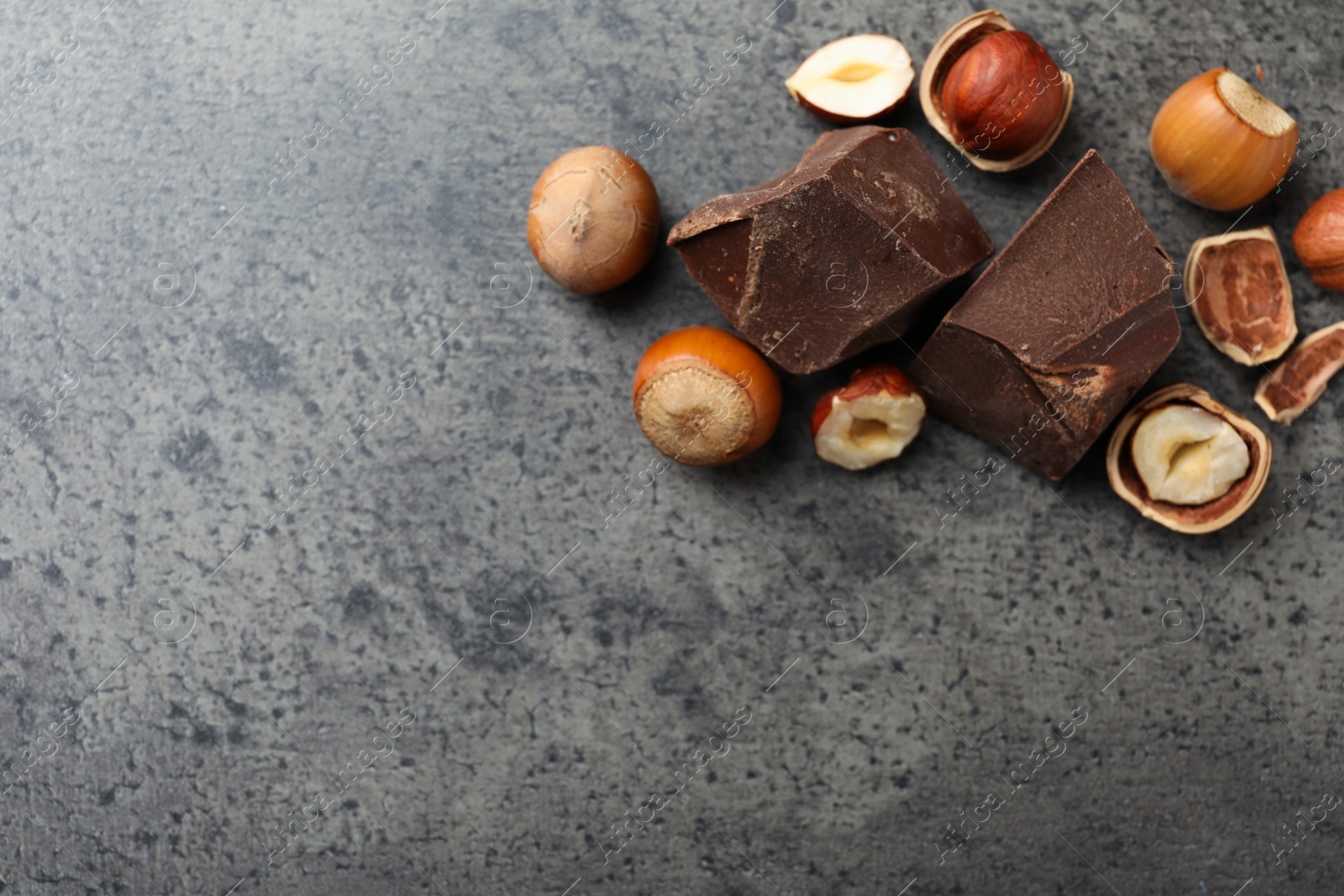 Photo of Delicious chocolate chunks and hazelnuts on grey table, flat lay. Space for text