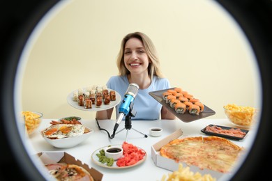Photo of Food blogger eating at table against beige background, view through ring light. Mukbang vlog