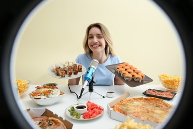 Food blogger eating at table against beige background, view through ring light. Mukbang vlog